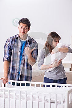 The young parents with their newborn baby near bed cot