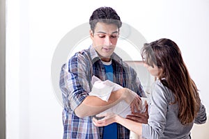 The young parents with their newborn baby near bed cot