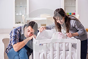 The young parents with their newborn baby near bed cot