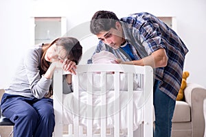 The young parents with their newborn baby near bed cot