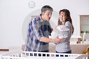 The young parents with their newborn baby near bed cot