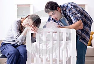 Young parents with their newborn baby near bed cot