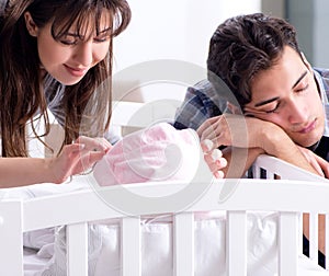 Young parents with their newborn baby near bed cot