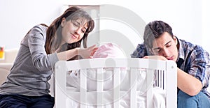 Young parents with their newborn baby near bed cot