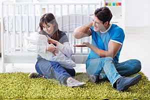 The young parents with their newborn baby sitting on the carpet