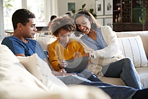 Young parents and their pre-teen daughter sitting on a sofa in the living room using a tablet computer together, selective focus