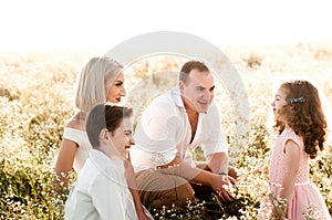 Young parents with their son and daughter are sitting in a daisy field
