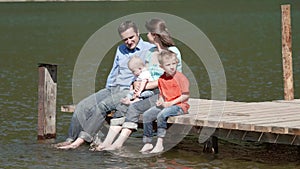 Young parents with two children on pontoon, family barefoot admiring nature, little brothers with mother and father in holiday
