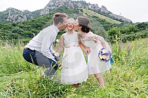 Young parents in wedding dresses kiss their young daughter in cheeks