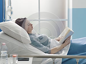 Young patient lying in a hospital bed and reading a book