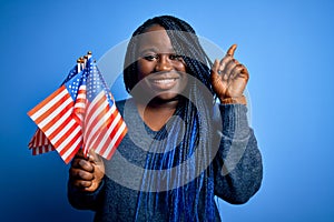 Young patriotic african american plus size woman with braids holding united states flags surprised with an idea or question