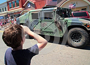 Young patriotic boy salutes military in July 4th parade.