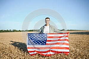 Young patriotic farmer stands among new harvest. Boy walking with the american flag on the wheat field celebrating