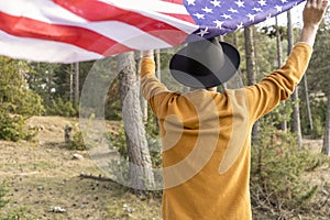 Young patriotic man in cowboy hat waving United States American flag in forest.Beautiful woodland landscape at sunset.Independence