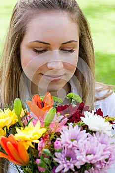 Young peaceful woman smelling a bunch of flowers while closing h