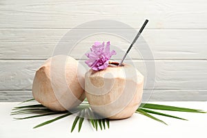 Young peeled coconuts with straw, palm leaf and flower on white wooden table