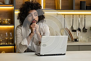 Arabian man works remotely on computer at table in kitchen