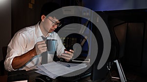 Young pensive asian man working late concentrated and serious in front of computer at night in dark office, Late night working or