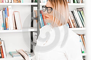 Young pensive attractive woman in formal clothes reading a book at library