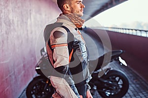 Young pensive biker is standing near his motobike in quiet tunnel