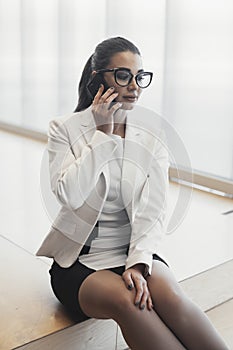 Young pensive business woman in white jacket talking by mobile phone.