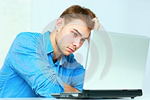 Young pensive businessman sitting at the table with laptop
