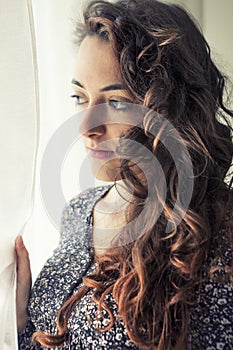 Young pensive girl near the white curtain of a window