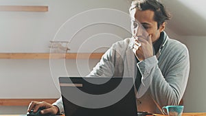 Young pensive man with tousled hair works on laptop. Hard worker. Efficiency.