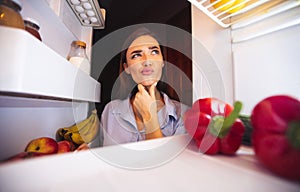 Young pensive woman thinking near opened fridge