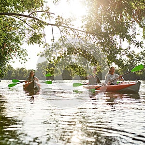 Young people boating together in river surrounded by trees at spring or summer, spending time together outdoors