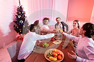 Young People Clinking Glasses Toasting During Christmas Dinner In Restaurant