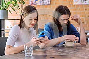 Young people, couple man and woman relaxing together in cafe, using smartphone