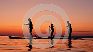 Young people are crossing sunset lake on paddleboards