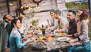 Young people dining and having fun drinking red wine together on balcony rooftop dinner party - Happy friends eating bbq food at