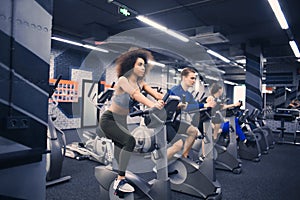 Young people doing exercises on elliptical trainer in gym