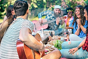 Young people doing picnic and playing guitar in park - Group of happy friends having fun during the weekend outdoor