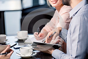Young people drinking coffee and writing in notebooks at business meeting, business lunch concept