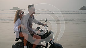 Young people drive motorbike on sea beach at sunset. Man, woman travel by motorcycle on coastline along ocean. Female
