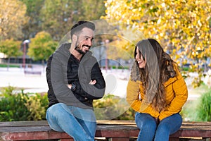 Young people on a first date sitting on a wooden bench in a park and laughing