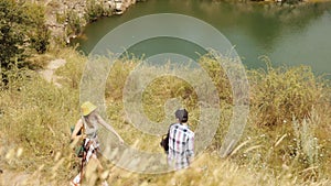 Young people, friends, men and women in comfortable clothes going hiking, walking down the hill with beautiful river