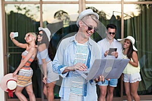 Young People Group On Terrace Tropical Hotel, Friends Using Cell Smart Phone Tropic Holiday Vacation