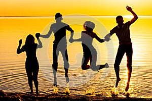 Young people, guys and girls, are jumping against the sunset background, silhouettes