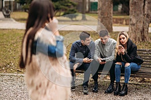 Young people having a good time in park. Male and female sitting on the bench and using phones