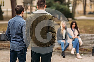 Young people having a good time in park. Male and female sitting on the bench and using phones