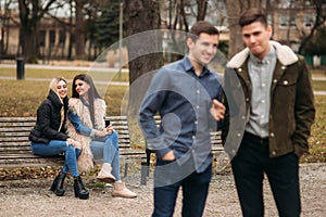 Young people having a good time in park. Male and female sitting on the bench and using phones