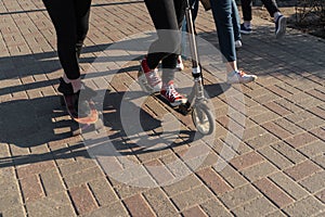 Young people in jeans and sneakers skating and using a scooter on a concrete brick pavement