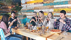 Young people photographing food in rustic restaurant â€“ happy friends taking picture of pizza and hamburgers with mobile phones