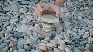 Young people play on the beach and put stones on top of each other. They build a pebble turret close-up.