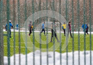 Young people play football in the snow in winter. View through fence. Leisure, active outdoor plays, sport. Selective