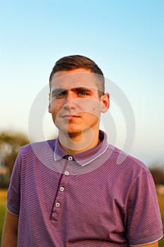 Young people.Portrait of serious young brunette man in purple polo shirt standing outdoor on nature background at summer